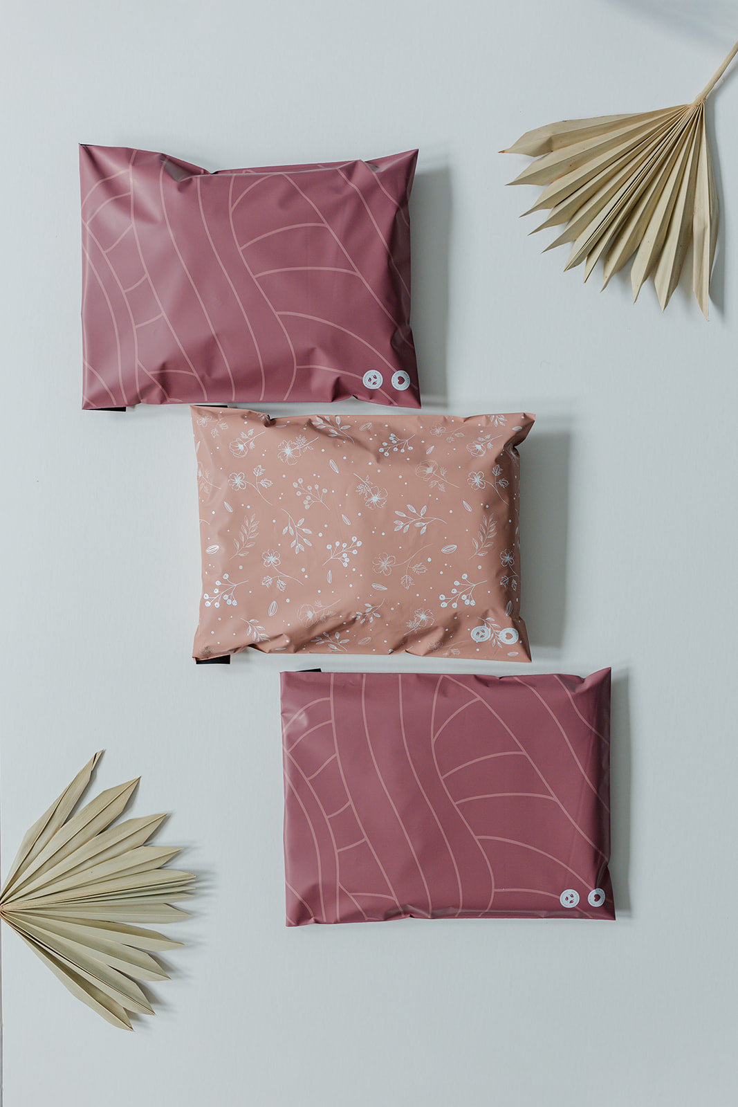 Three Copper Rose Leaf Biodegradable Mailers 10" x 13" with palm leaves on a recyclable surface from impack.co.