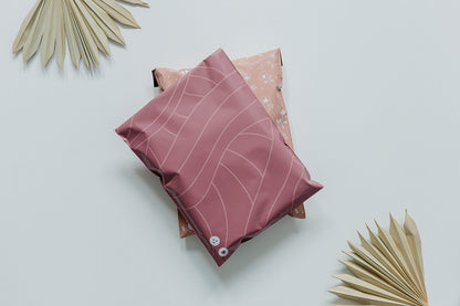 A recyclable Copper Rose Leaf Biodegradable Mailers 10" x 13" pillow and a palm leaf on a white surface, by impack.co.