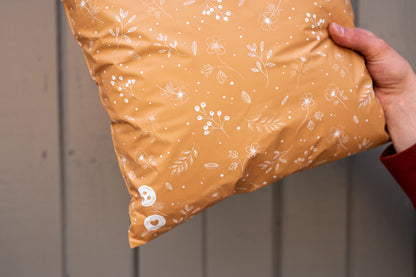 A person holding a Floral 2D Chestnut Biodegradable Mailers 12" x 15.5" pillow from impack.co with a floral pattern on it.