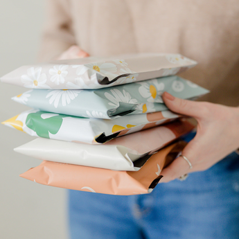 A person holding a stack of five neatly wrapped packages, each with different floral and geometric designs.