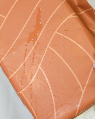 Water beads and runs off the surface of an orange waterproof fabric with a light geometric pattern, demonstrating its water-resistant property.