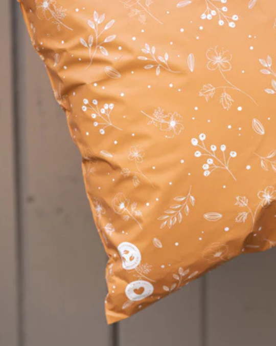 Close-up of a mustard yellow pillow with white floral and plant patterns, leaning against a light wooden surface.