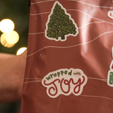 A close-up of a red gift bag decorated with impack.co Christmas Thank You Stickers, featuring festive designs like a Christmas tree and cheerful messages—perfect for holiday gift wrapping.