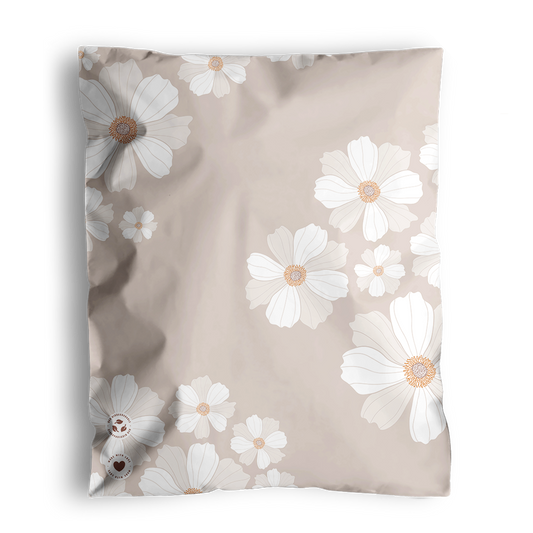 A floral-patterned pillow on an impack.co Cosmos Biodegradable Mailers 10" x 13" surface, with the corner of a geometric-patterned piece partially visible in the background.