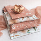 A set of Floral 2D Rosy Brown Biodegradable Mailers 10" x 13" recyclable gift bags by impack.co on a bed.