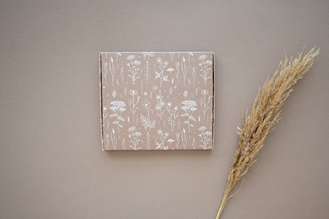 A SlimBox Wildflower 7" x 8" - Large notebook from impack.co with a flower pattern on it and a stalk of grass next to it.