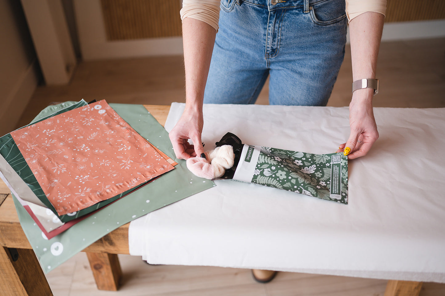A woman is sewing a piece of fabric on a table using the impack.co Emerald Evergreen Biodegradable Mailers 6" x 9".