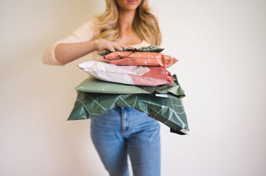 A person holding a stack of impack.co Olive Leaf Biodegradable Mailers 14.5" x 19" with one hand, featuring a charming Olive Leaf print.