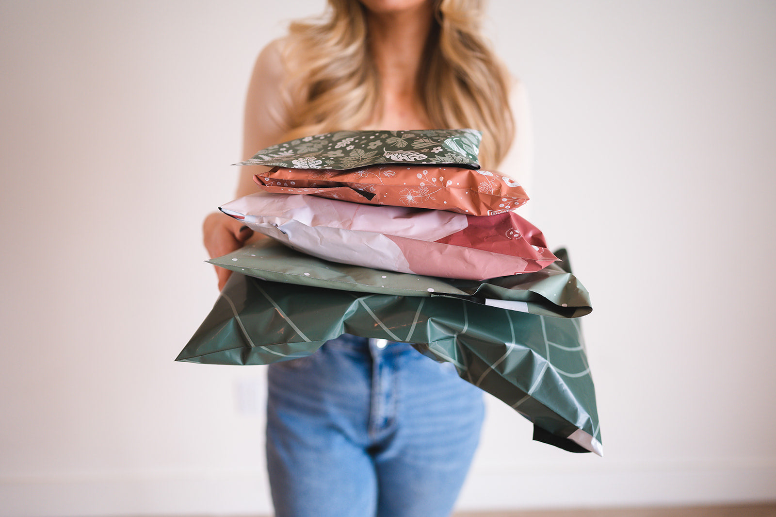 A woman holding a stack of Olive Leaf Biodegradable Mailers 14.5" x 19" from impack.co wrapping paper.