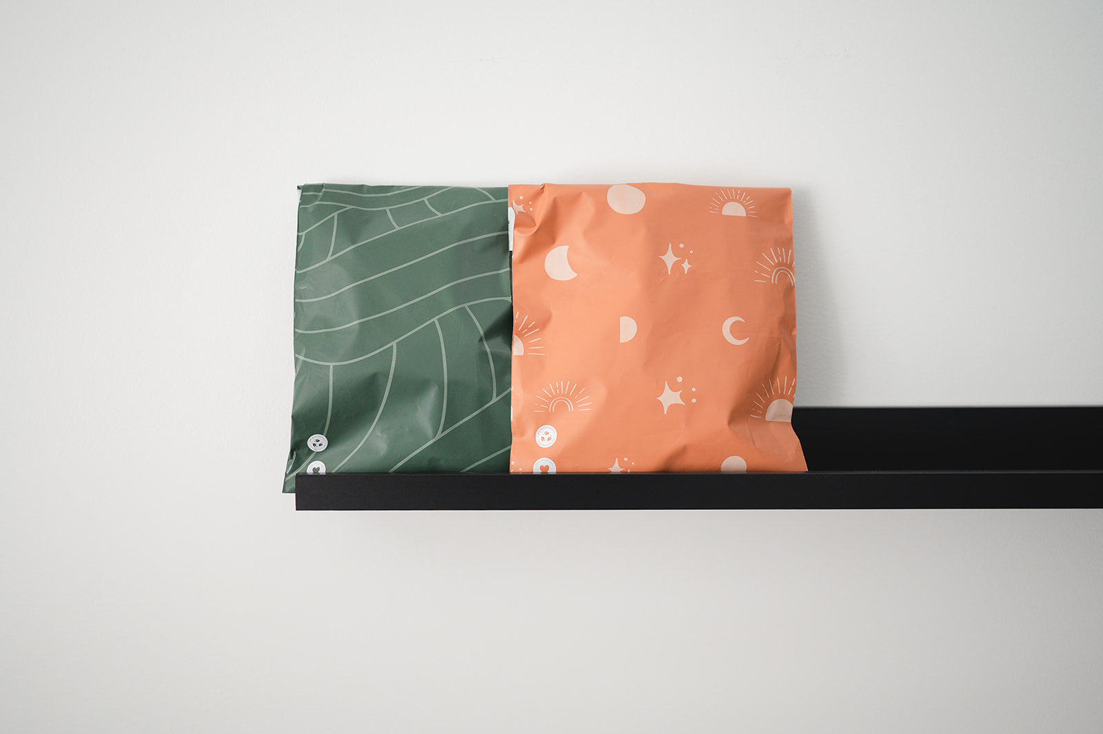 A green and orange Olive Leaf Biodegradable Mailers 10" x 13" bag sitting on a shelf, by impack.co.
