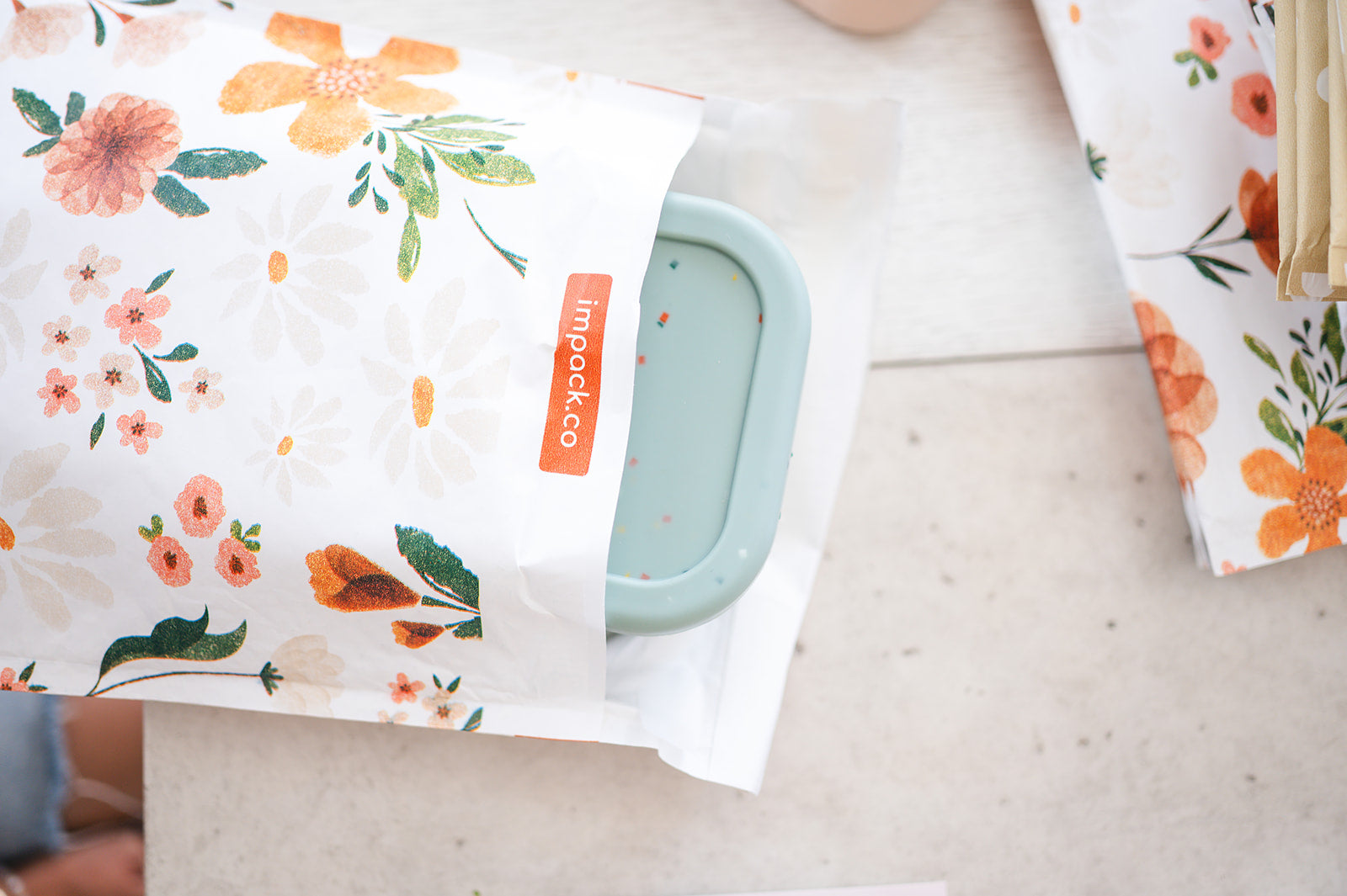 A person is sitting on a table with an impack.co eco-friendly bag decorated with flowers, enhancing the brand's image as environmentally conscious.