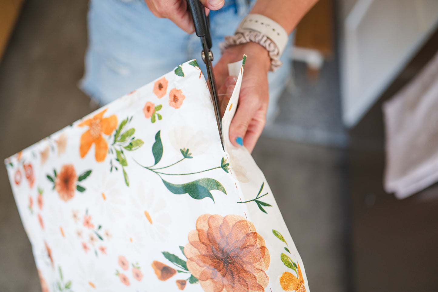 A woman is cutting a fabric with a floral pattern for Gardenlumina Padded Paper Mailers 10" x 13" from impack.co.