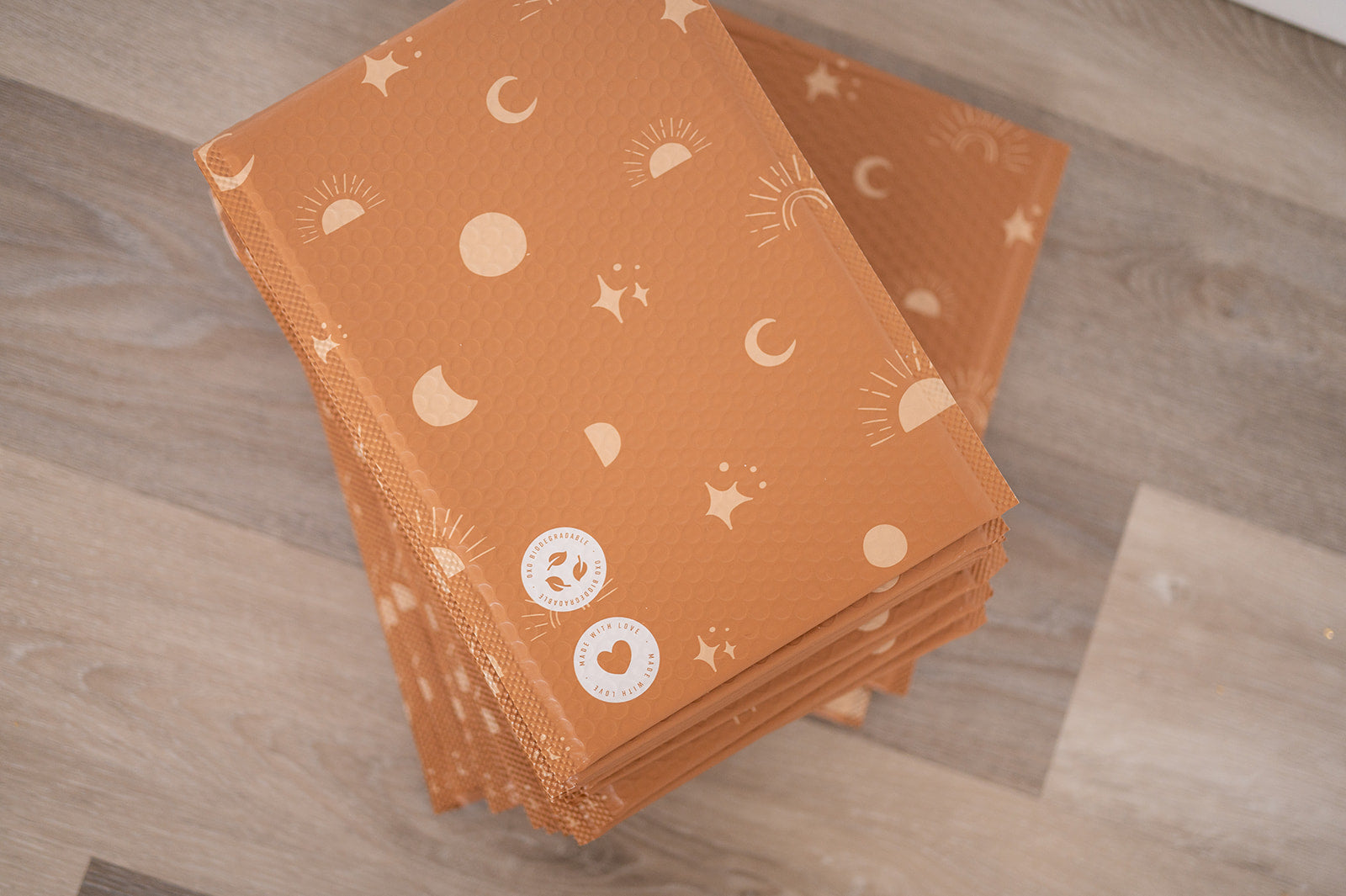 A stack of Celestial Tan Biodegradable Bubble Mailers 8.5" x 12" from impack.co on a wooden floor.