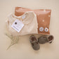 A baby's clothes and shoes are laid out on a table, while the Celestial Tan Biodegradable Bubble Mailers 8.5" x 12" from impack.co make it easy to pack up and send off your shipments.
