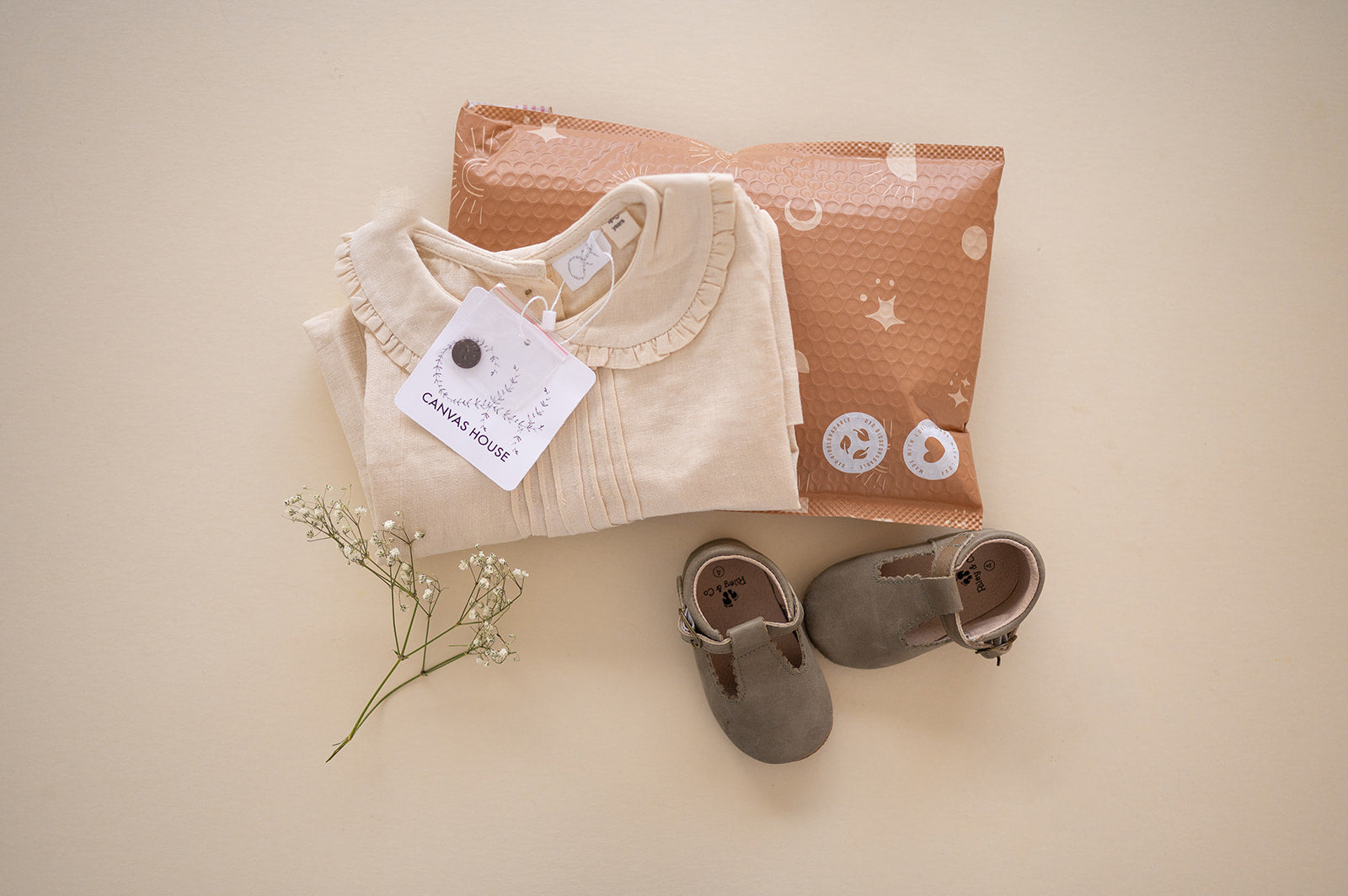 A baby's clothes and shoes are laid out on a table, while the Celestial Tan Biodegradable Bubble Mailers 8.5" x 12" from impack.co make it easy to pack up and send off your shipments.