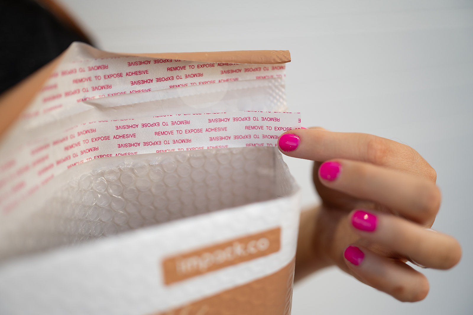 A person holding a bag with Celestial Tan Biodegradable Bubble Mailers 8.5" x 12" from impack.co materials and a secure adhesive strip to keep the products inside protected.