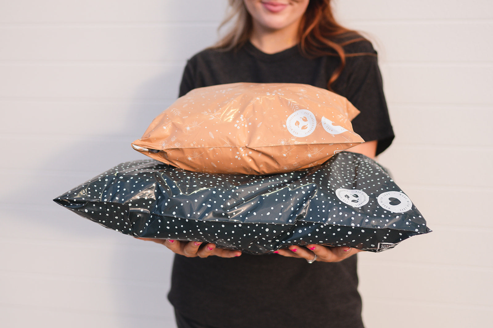 A woman holding two Floral 2D Chestnut Biodegradable Mailers 12" x 15.5" with recyclable polka dot patterns, from impack.co.