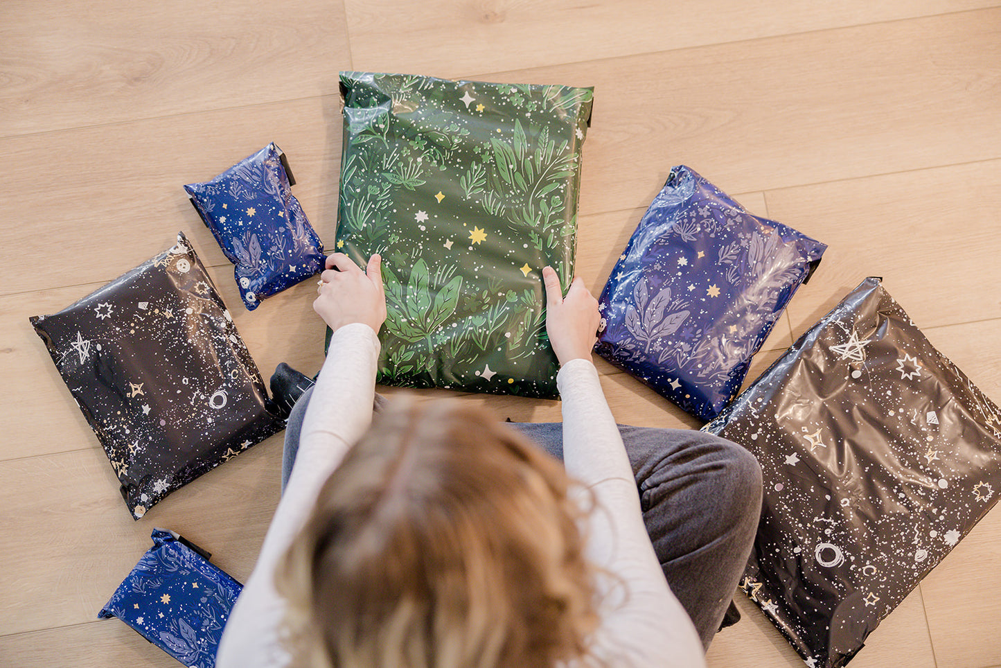 A woman is sitting on the floor with several Midnight Galaxy Mailers 10" x 13" bags from impack.co.