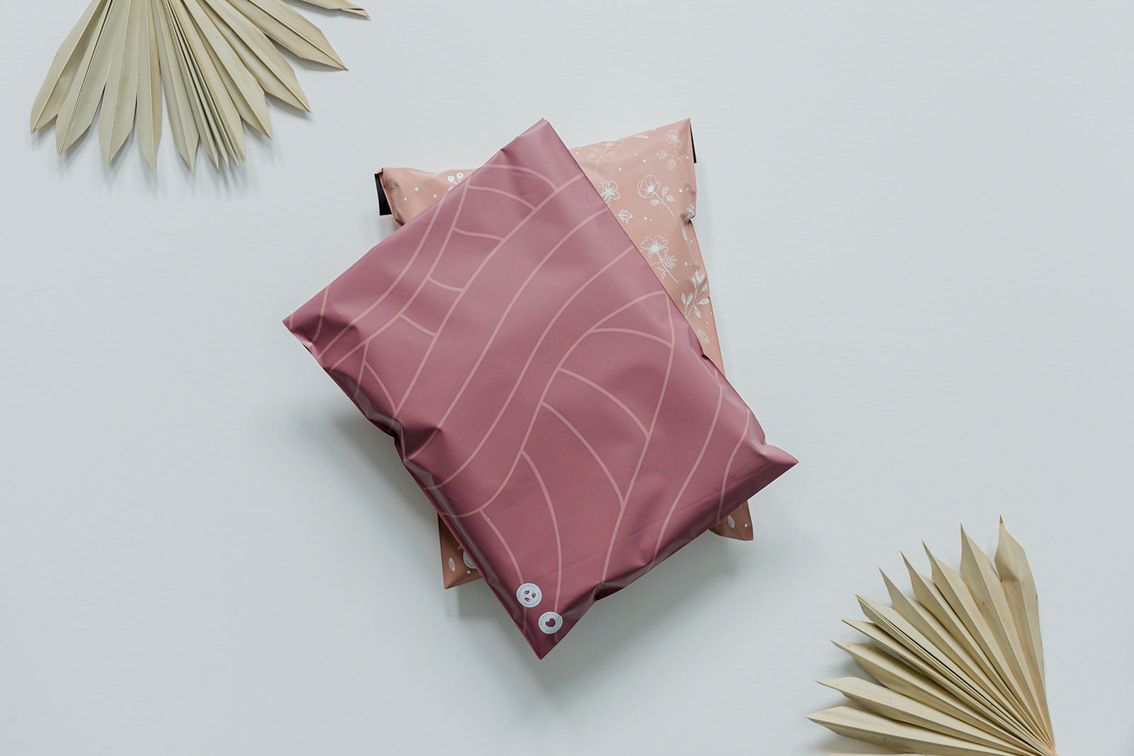 A recyclable Copper Rose Leaf Biodegradable Mailers 10" x 13" pillow and a palm leaf on a white surface, by impack.co.