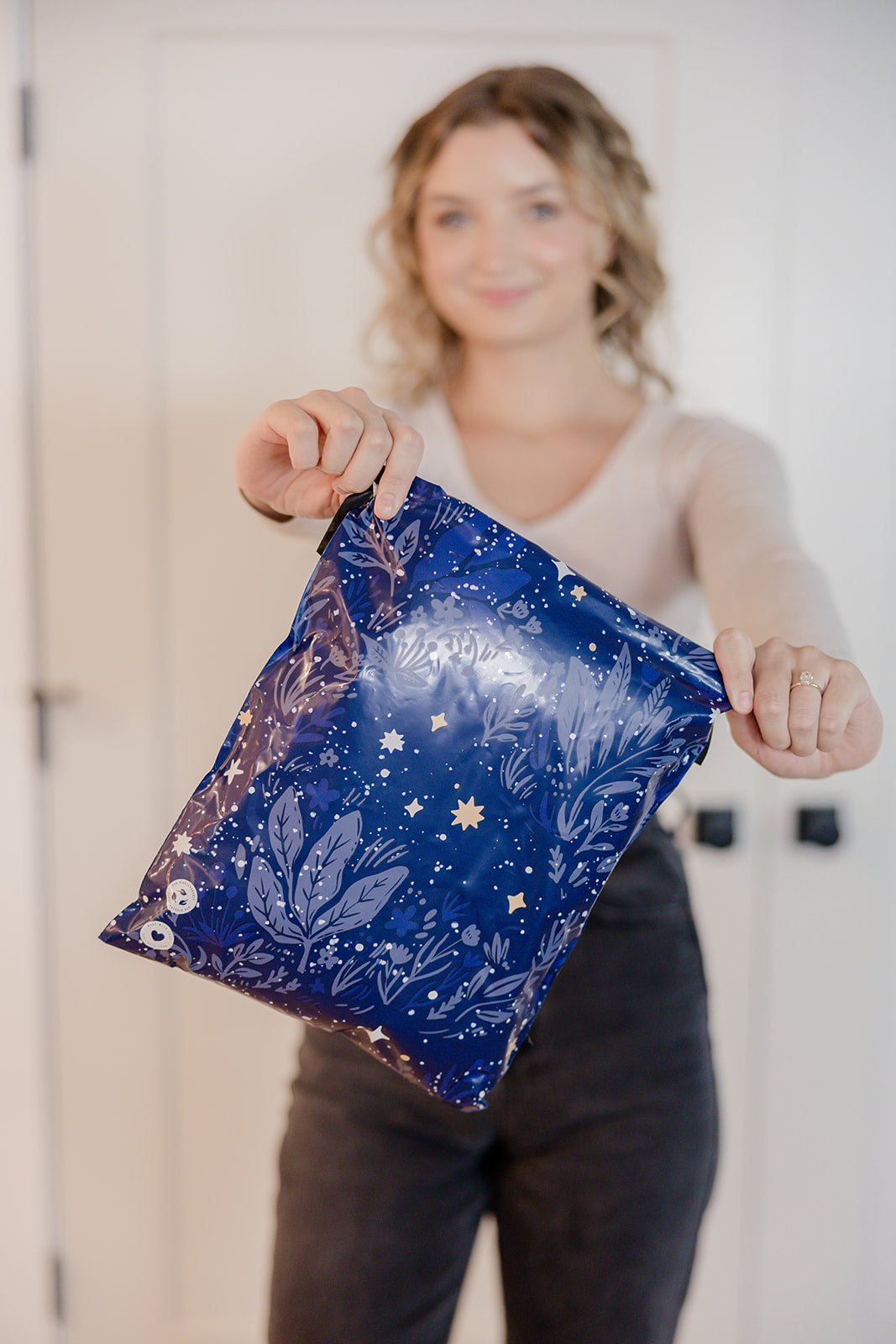 A woman holding up a Midnight Indigo Mailers 10" x 13" bag from impack.co.
