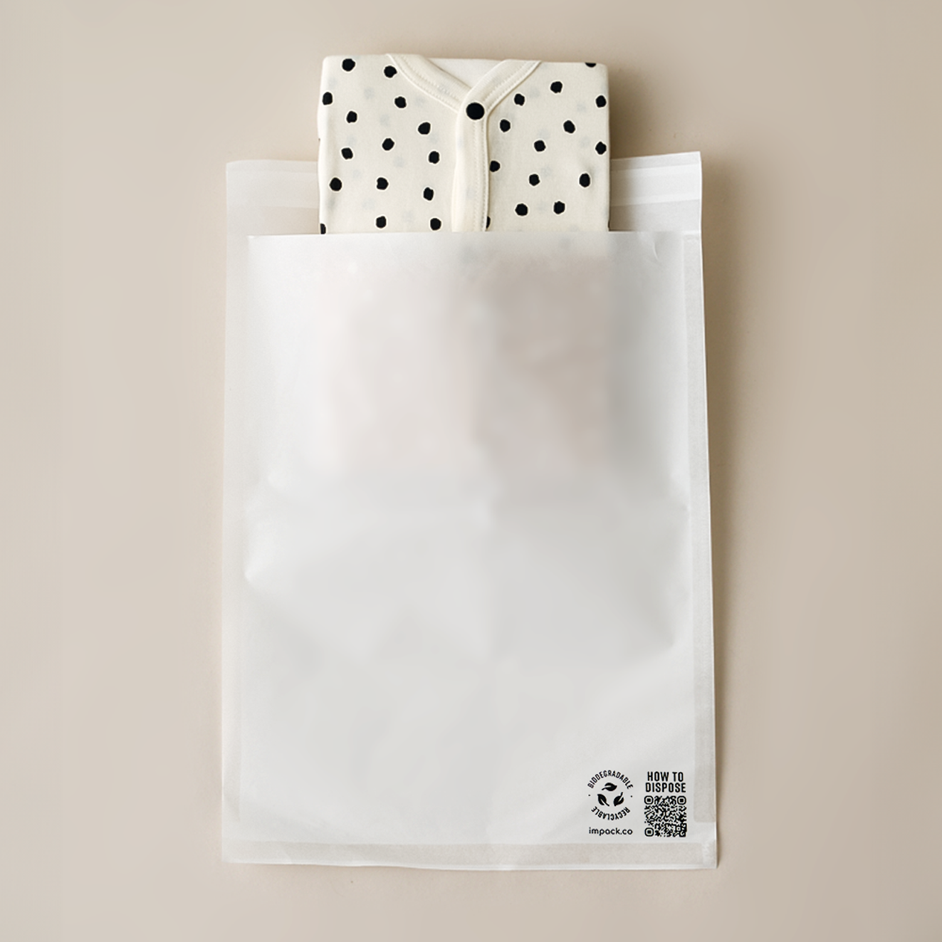 A white, partially transparent plastic packaging bag with recycling symbols and text on the front. A polka-dot fabric item is partially visible inside the impack.co Glassine Bags 9.6" x 12.6", protruding from the top.