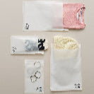 White and pink T-shirt, yellow beanie, black and white scarf, silver rings, and two geometric earrings are arranged on a light beige surface, each item partially inside translucent impack.co Glassine Bags 9.6" x 12.6".