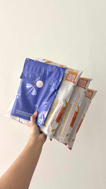 A hand holds four impack.co mailers—three are white with orange accents, while one is a Boho Sun & Moon Biodegradable Mailer (14.5" x 19"), perfect for shipping bulkier items sustainably.