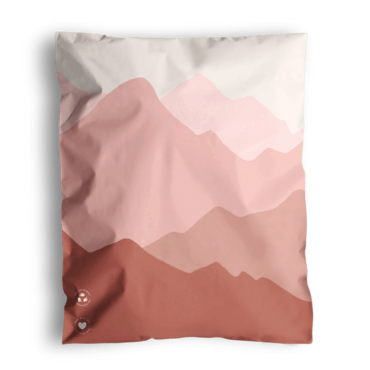 A graphic print cushion with a mountain landscape design in shades of pink and white, shipped in impack.co Mountain Clay Mailers 10" x 13".