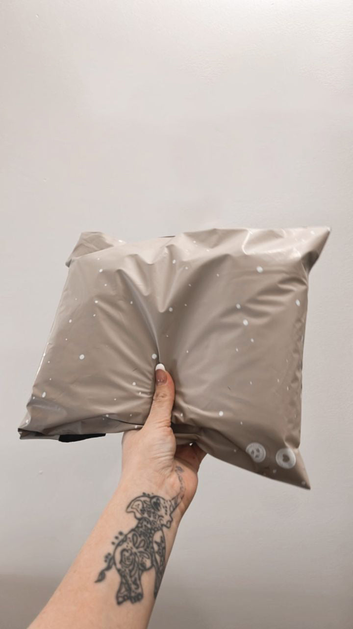 A person holding a Sandstone Biodegradable Mailers 10" x 13" pillow with a tattoo on it branded by impack.co.
