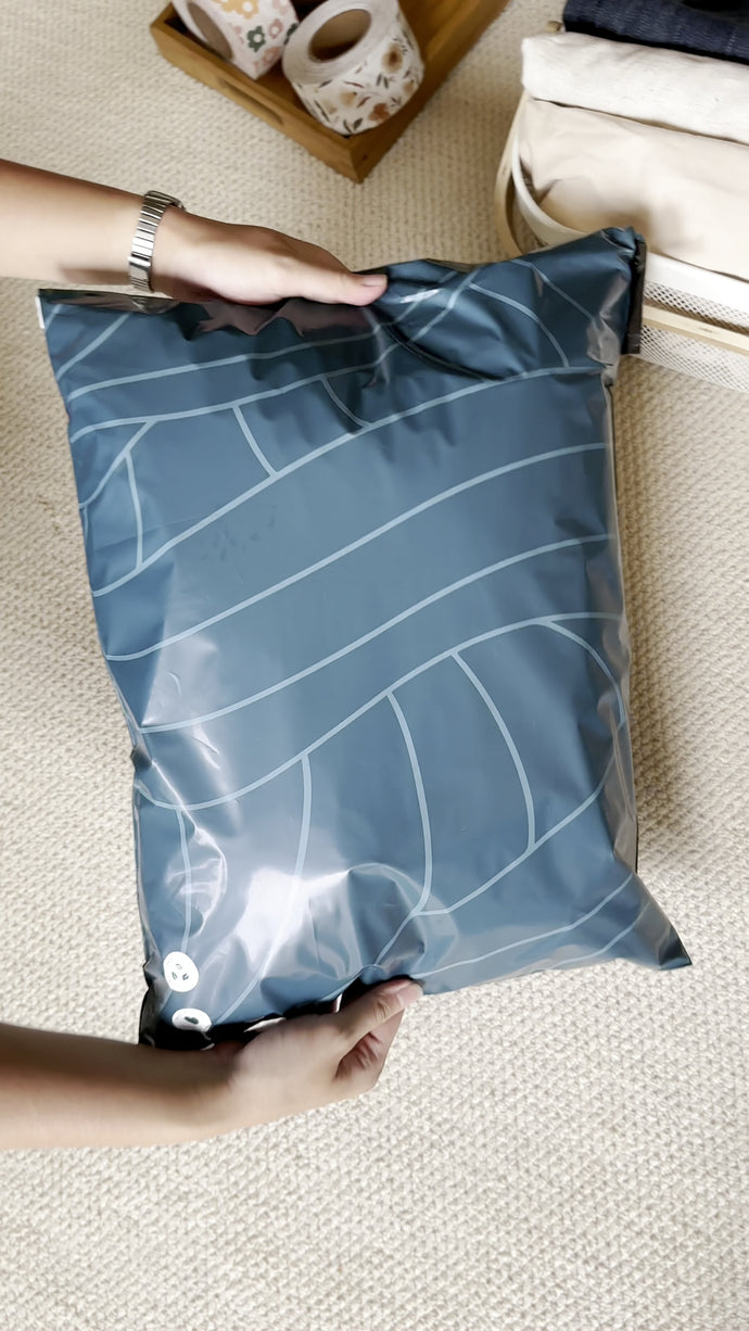 A person holds a large blue-gray vacuum storage bag with white lines, placed on a light-colored carpeted floor.