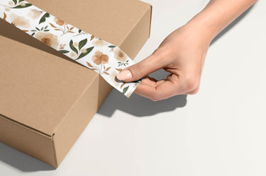 An eco-friendly hand unwrapping a brown box with floral tape.