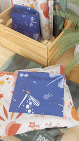 Impack.co’s Boho Sun & Moon Biodegradable Mailers (10" x 13") featuring vibrant, celestial designs are displayed on a wooden surface and in a box with a fern—ideal for adding a touch of boho style to your packaging.