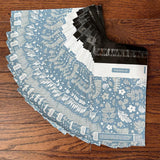 A stack of Sapphire Evergreen Biodegradable Mailers 10" x 13" envelopes from impack.co on a wooden floor.