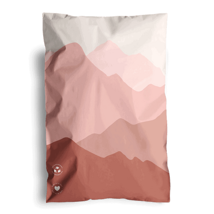 A graphic printed pillow with a mountain landscape design in pink shades, packaged in impack.co's Mountain Clay Mailers 6" x 9".