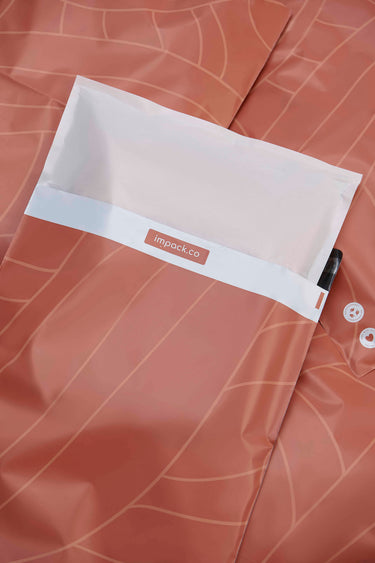 A Glassine Bag from impack.co lies on a textured leaf-patterned surface, symbolizing a shift to eco-friendly alternatives. Partially visible are two buttons and a small black item, blending practicality with sustainability.