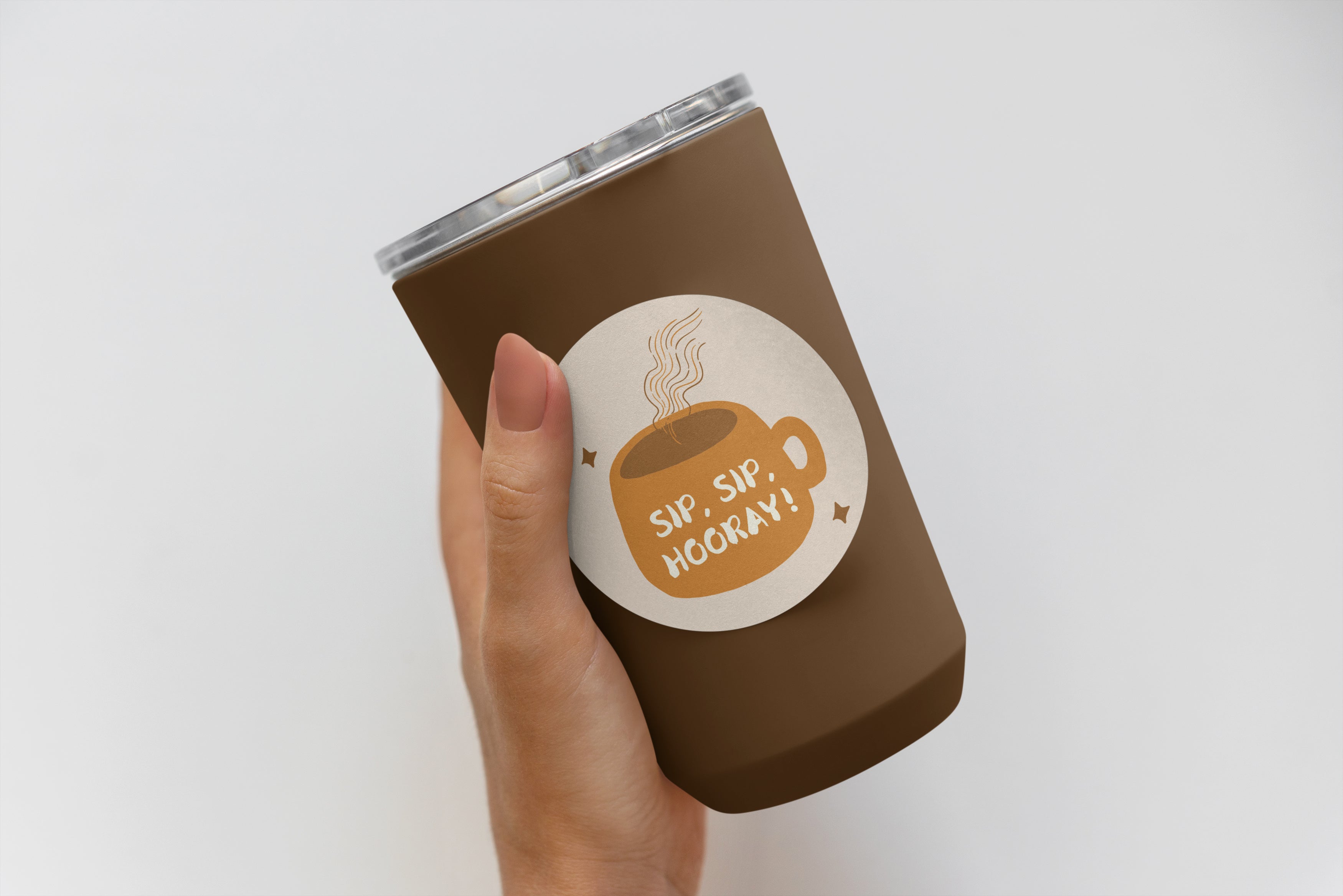 A hand holds a brown tumbler with a lid featuring an impack.co Custom Vinyl Die Cut Sticker that depicts a steaming cup and the text "SIP, SIP HOORAY!".