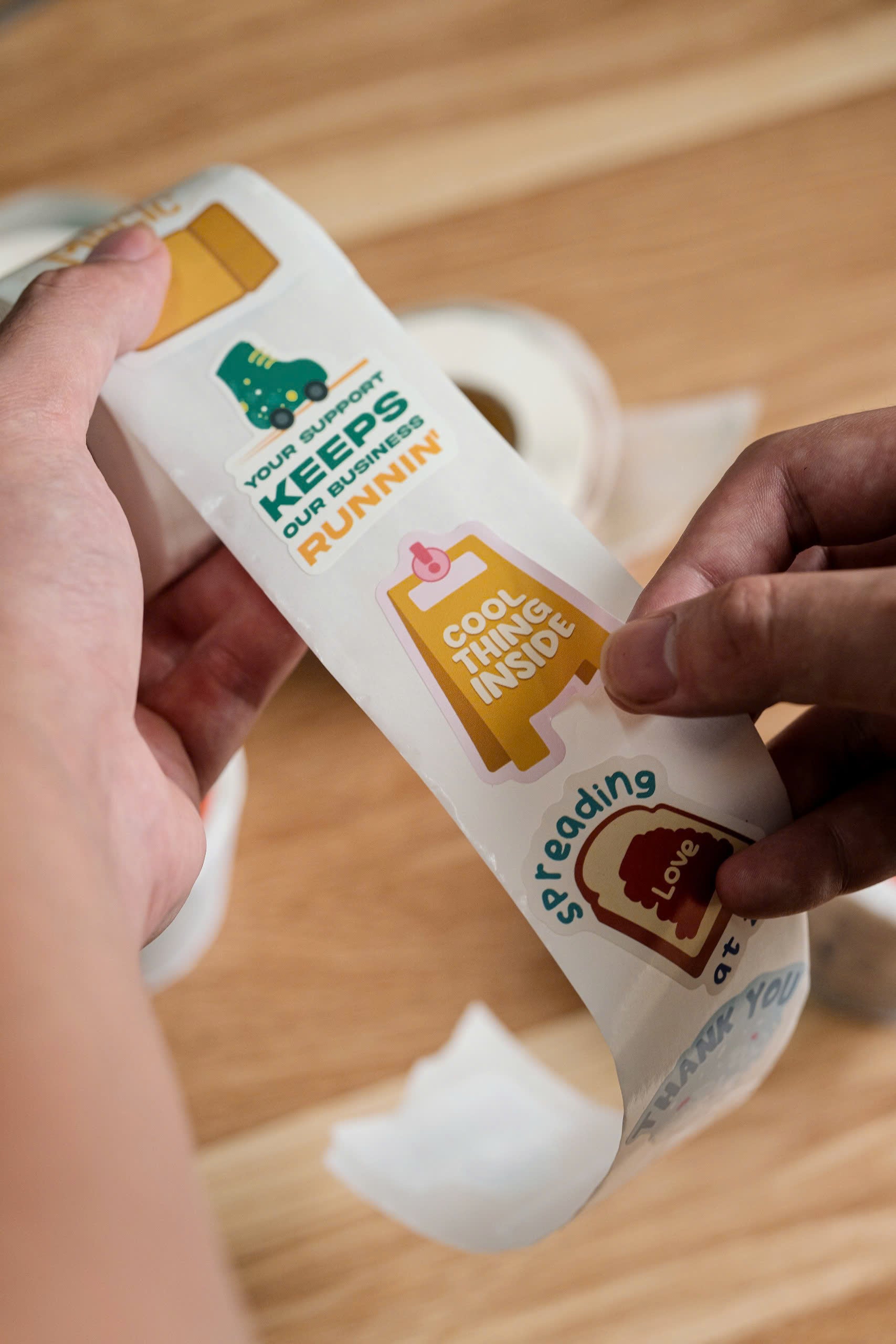 A person holds a strip of colorful stickers with motivational phrases and cute icons over a wooden surface.