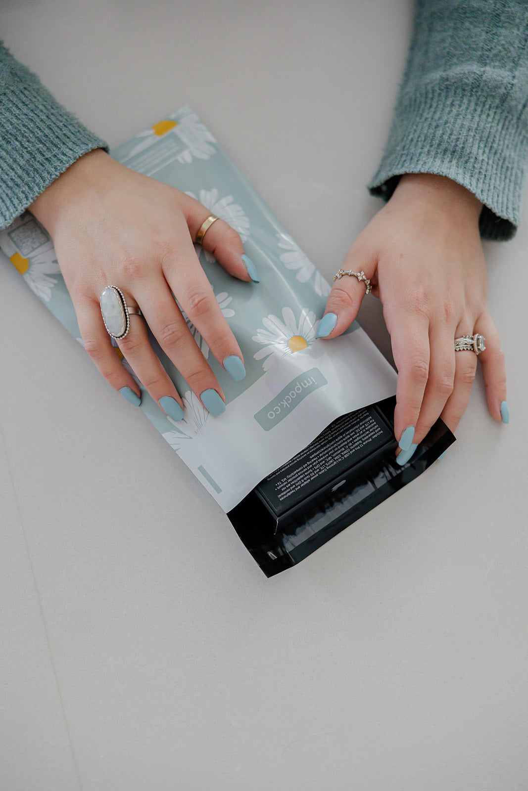 A woman's hand is holding a bag of impack.co Daisy White Biodegradable Mailers 6" x 9".