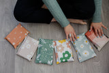 A person sits calmly on the floor, organizing six impack.co SALE - Cosmos Biodegradable Mailers 6" x 9", each featuring eye-catching patterns. These mailers combine style with transit protection, providing an eco-friendly touch to mailing needs.