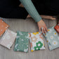 A woman is sitting on a wooden floor with a bunch of different colored impack.co Biodegradable Mailers 10" x 13" pouches.