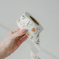 A person holding a roll of Packing Tape - Camelia Bloom from impack.co with a floral pattern.