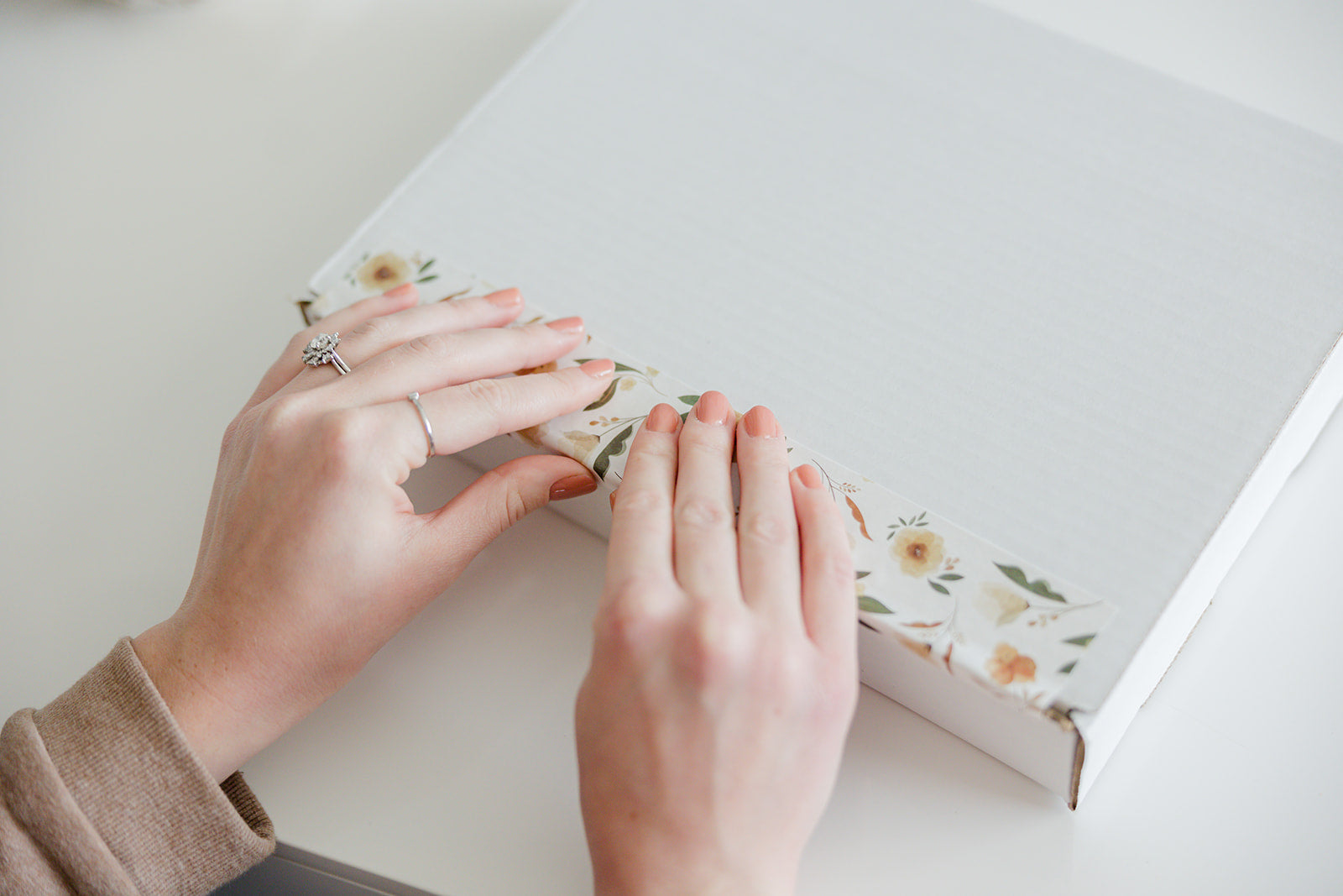 A woman's hands are opening up a white box sealed with Packing Tape - Camelia Bloom from impack.co.