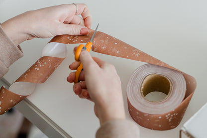 A person cutting a roll of Packing Tape - Floral Rosy Brown with scissors from impack.co.