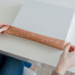 A woman is wrapping Packing Tape - Floral Rosy Brown from impack.co around a box on a table.
