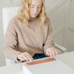 A woman sitting at a desk with a box of impack.co Packing Tape - Floral Rosy Brown in front of her.