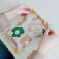 A woman is holding a bag with Daisy Multicolor Biodegradable Mailers 10" x 13" from impack.co with flowers on it.