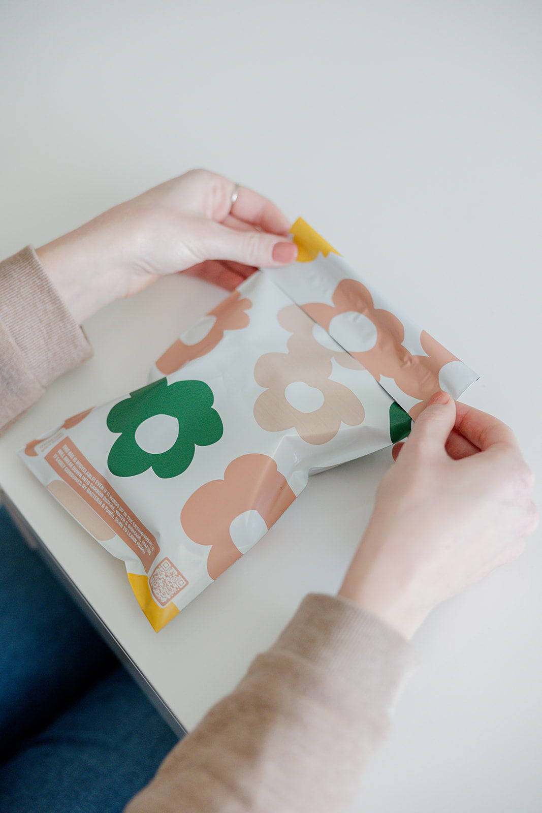 A woman is holding a Daisy Multicolor Biodegradable Mailers 6" x 9" bag from impack.co with flowers on it.