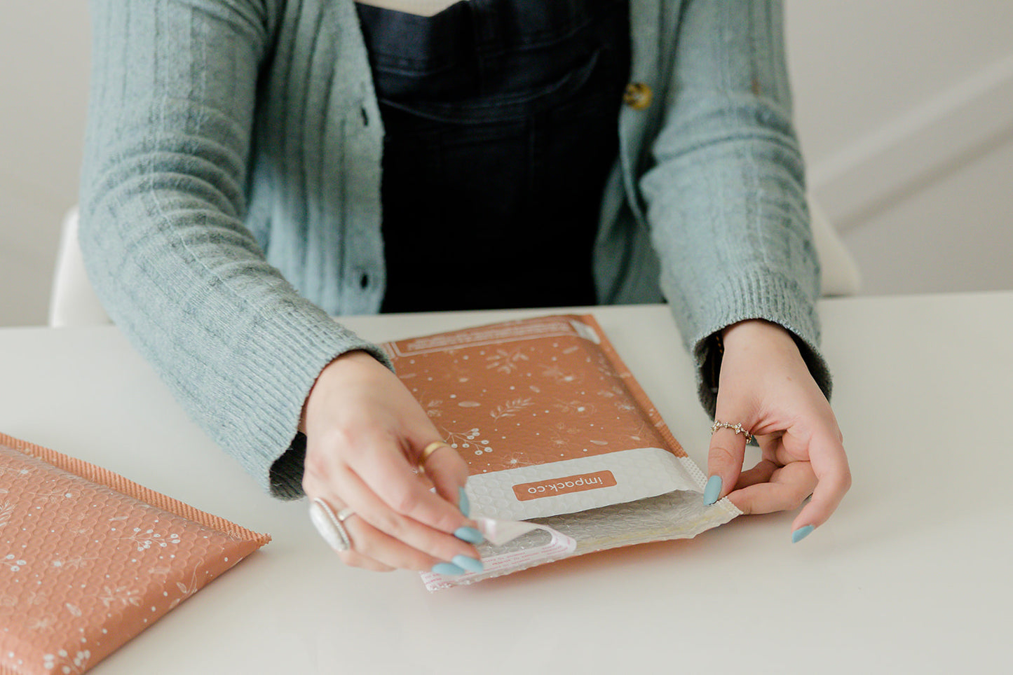 A woman is putting a Rosy Brown Biodegradable Bubble Mailer 6" x 9" from impack.co on a table.
